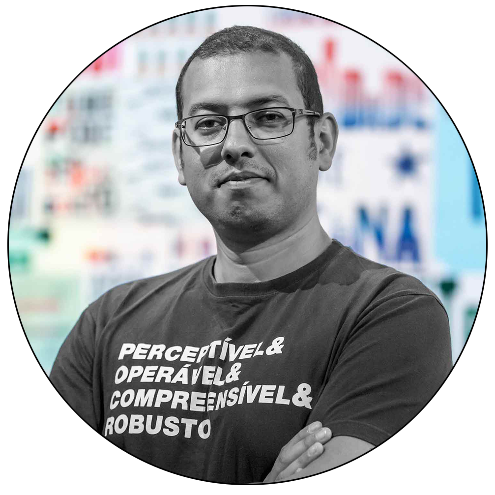 Foto redonda contemplando apenas o meu rosto. O fundo é um céu azulado. Uso óculos e fones de ouvido. Cachecol em tom cinza escuro e blusa de couro marrom. Possuo barba semi-serrada e cabelo bem curto. Olhos castanhos escuros e olhar fixo para a câmera.